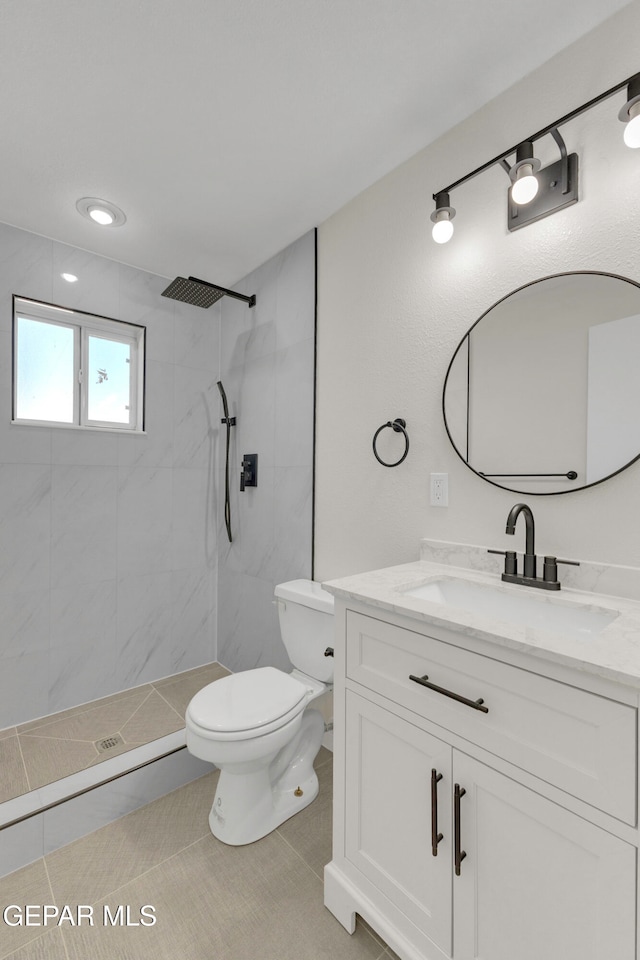 bathroom with toilet, vanity, a tile shower, and tile patterned flooring