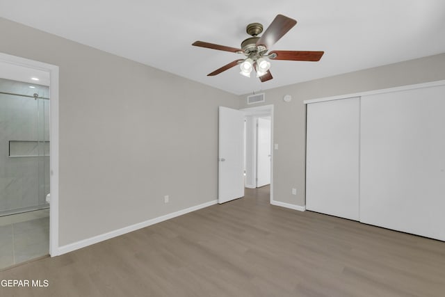 unfurnished bedroom featuring ceiling fan, ensuite bathroom, a closet, and hardwood / wood-style flooring