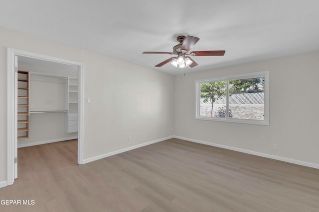 unfurnished bedroom with a walk in closet, a closet, light wood-type flooring, and ceiling fan