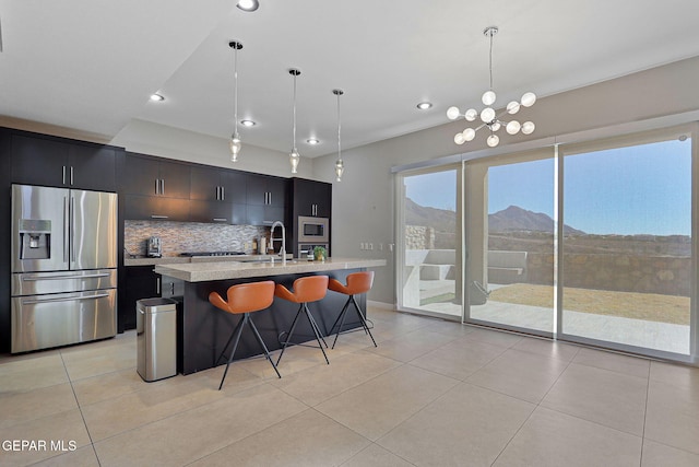 kitchen with a mountain view, appliances with stainless steel finishes, decorative light fixtures, and a center island with sink