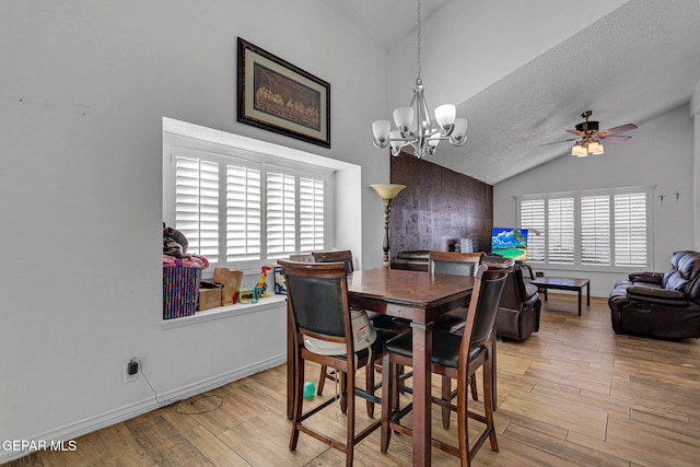 dining space featuring light hardwood / wood-style flooring, a textured ceiling, vaulted ceiling, and ceiling fan with notable chandelier