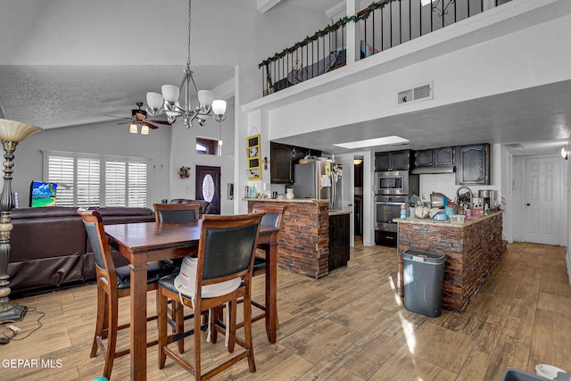 dining area featuring a textured ceiling, high vaulted ceiling, wood-type flooring, and ceiling fan with notable chandelier