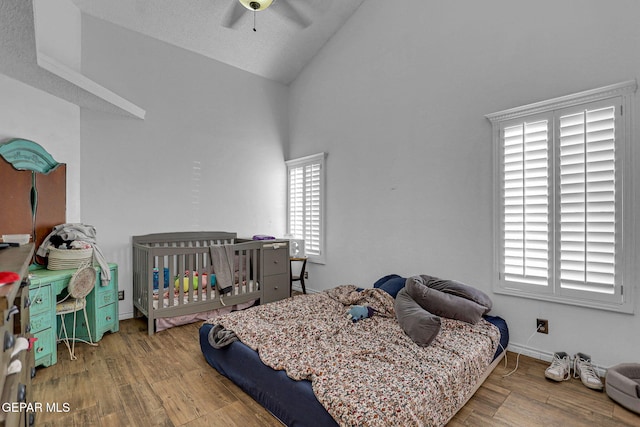 bedroom with lofted ceiling, a crib, hardwood / wood-style floors, a textured ceiling, and ceiling fan