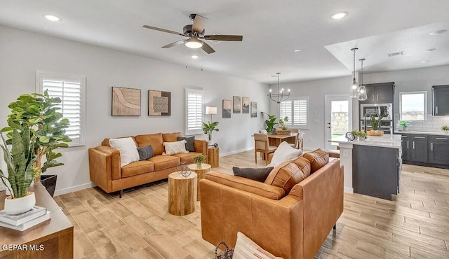 living room with a wealth of natural light, ceiling fan with notable chandelier, and light wood-type flooring