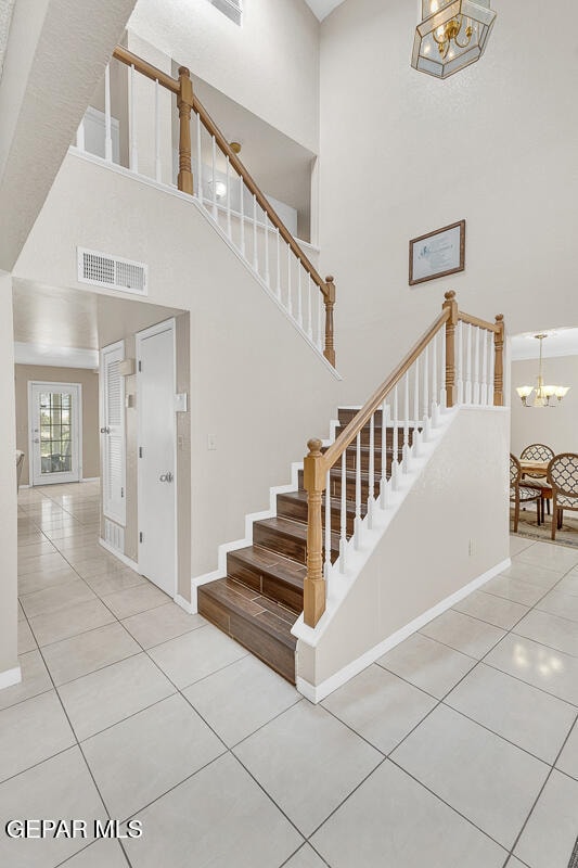 stairs with tile patterned floors, a high ceiling, and a chandelier