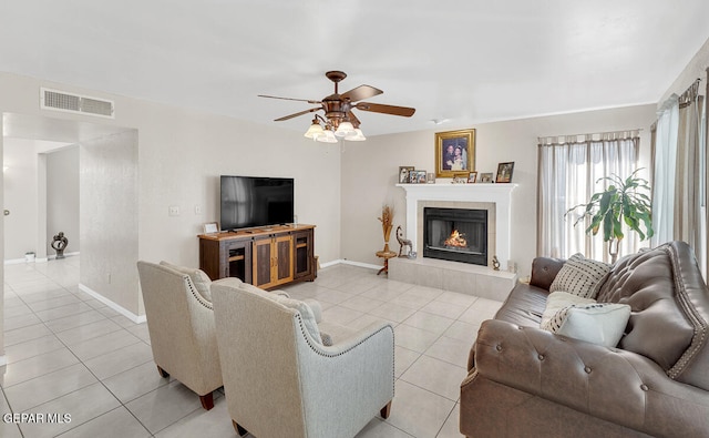 living room featuring ceiling fan, a tiled fireplace, and light tile patterned floors