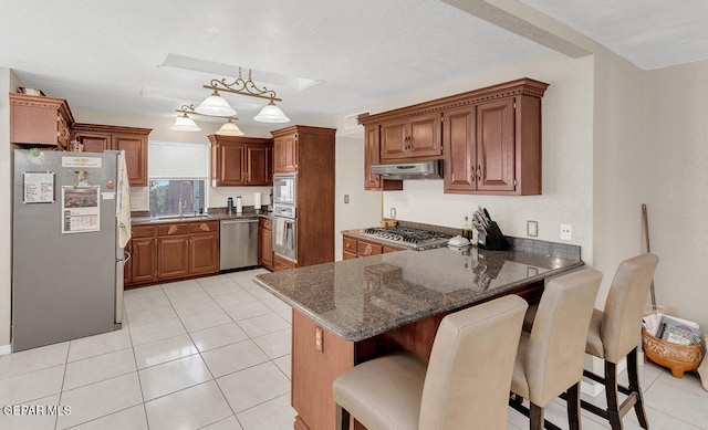 kitchen featuring appliances with stainless steel finishes, kitchen peninsula, dark stone countertops, extractor fan, and a breakfast bar area