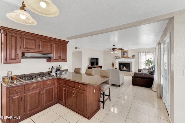 kitchen with kitchen peninsula, ceiling fan, a kitchen bar, light tile patterned flooring, and stainless steel gas cooktop