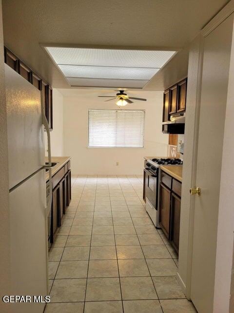 kitchen featuring gas range, ceiling fan, light tile patterned floors, and white refrigerator