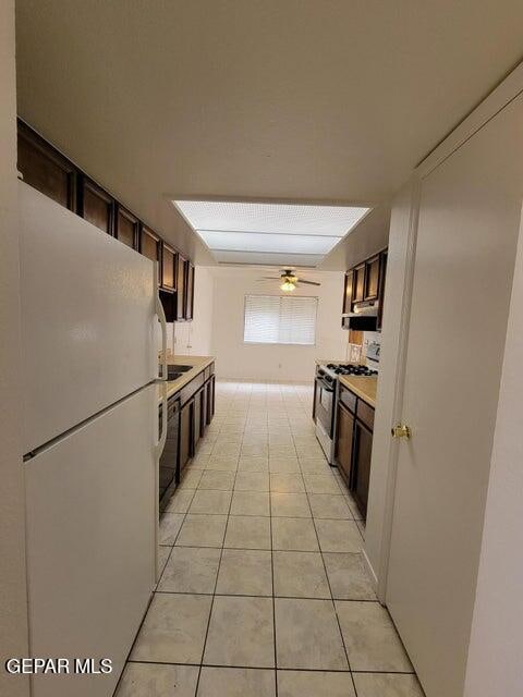 kitchen featuring light tile patterned floors, ceiling fan, white refrigerator, dark brown cabinetry, and stainless steel gas range