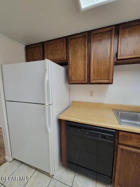 kitchen featuring black dishwasher, light tile patterned floors, and white refrigerator