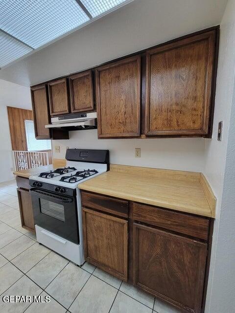 kitchen with white gas range, dark brown cabinets, and light tile patterned flooring