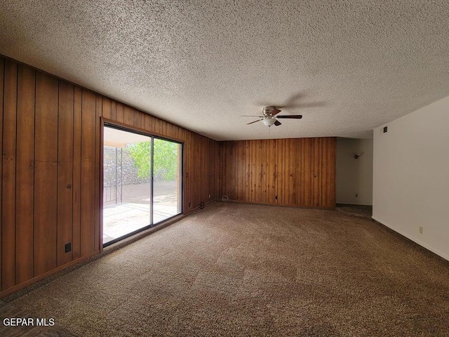 carpeted spare room with ceiling fan, a textured ceiling, and wood walls