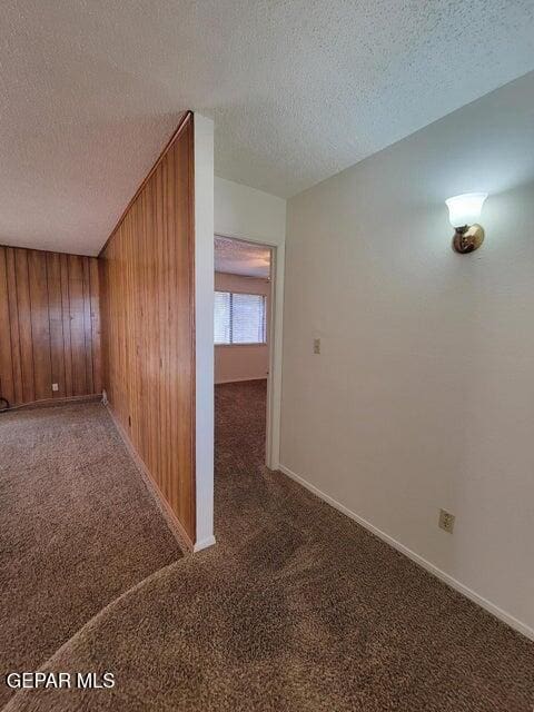 corridor with wood walls, a textured ceiling, and dark carpet