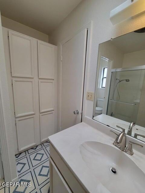 bathroom featuring toilet, a shower with shower door, and vanity