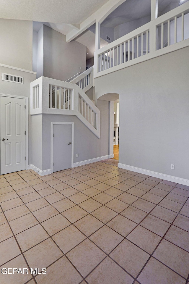 unfurnished living room with a textured ceiling, high vaulted ceiling, and light tile patterned floors