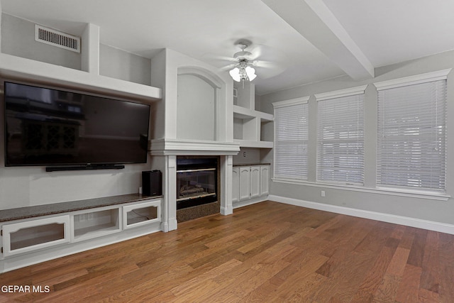 unfurnished living room featuring hardwood / wood-style floors, beamed ceiling, a fireplace, and ceiling fan