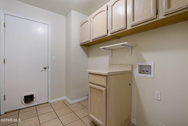 washroom with light tile patterned flooring, hookup for a washing machine, and cabinets