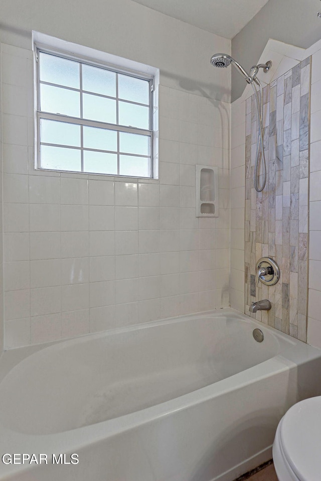 bathroom featuring a wealth of natural light, tiled shower / bath combo, and toilet