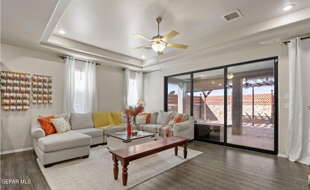 living room featuring a raised ceiling, ceiling fan, and dark hardwood / wood-style floors