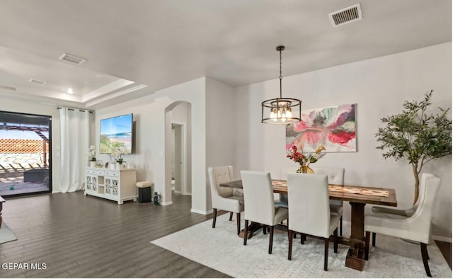 dining area featuring a raised ceiling, dark wood-type flooring, and a chandelier