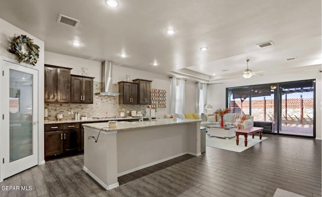 kitchen featuring a kitchen island with sink, dark hardwood / wood-style flooring, ceiling fan, and wall chimney range hood