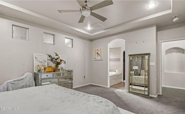 bedroom with a raised ceiling, ensuite bath, ceiling fan, and dark colored carpet