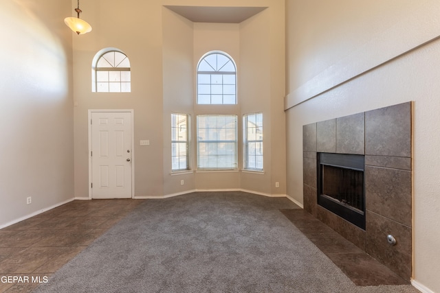 unfurnished living room featuring a towering ceiling, a fireplace, and dark colored carpet