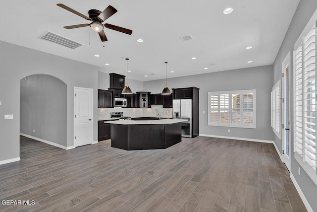 kitchen featuring decorative backsplash, hanging light fixtures, appliances with stainless steel finishes, dark hardwood / wood-style floors, and a center island