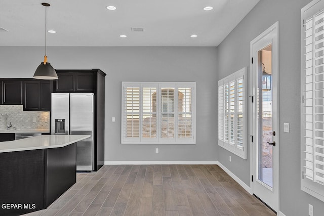 kitchen featuring backsplash, sink, stainless steel fridge, decorative light fixtures, and light wood-type flooring