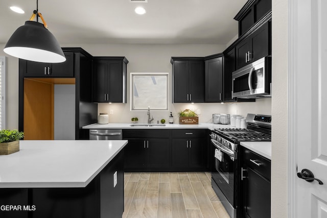 kitchen with appliances with stainless steel finishes, decorative light fixtures, sink, and light hardwood / wood-style floors