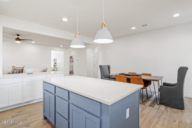 kitchen with light wood-type flooring, a center island, ceiling fan, pendant lighting, and white cabinets