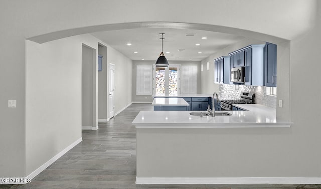 kitchen with kitchen peninsula, hanging light fixtures, stainless steel appliances, sink, and blue cabinets