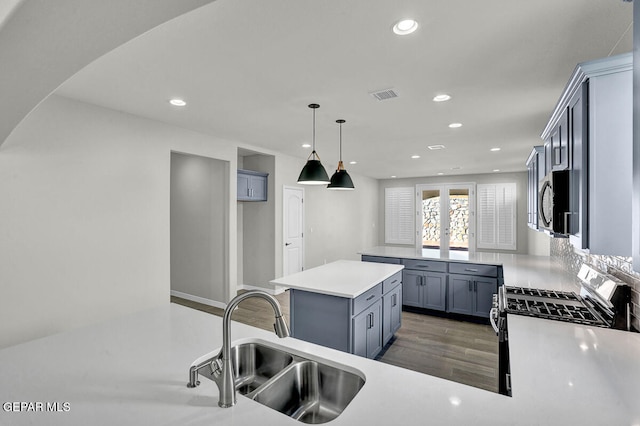 kitchen featuring gas range oven, sink, dark wood-type flooring, pendant lighting, and a center island