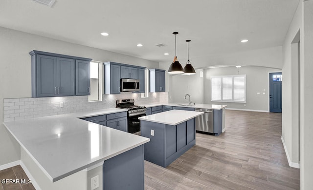 kitchen with a kitchen island, kitchen peninsula, pendant lighting, light wood-type flooring, and appliances with stainless steel finishes