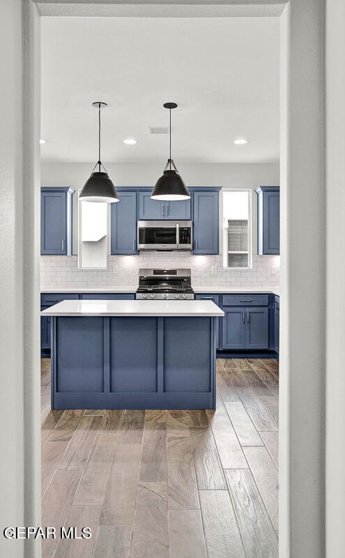 kitchen with backsplash, blue cabinetry, appliances with stainless steel finishes, and light wood-type flooring