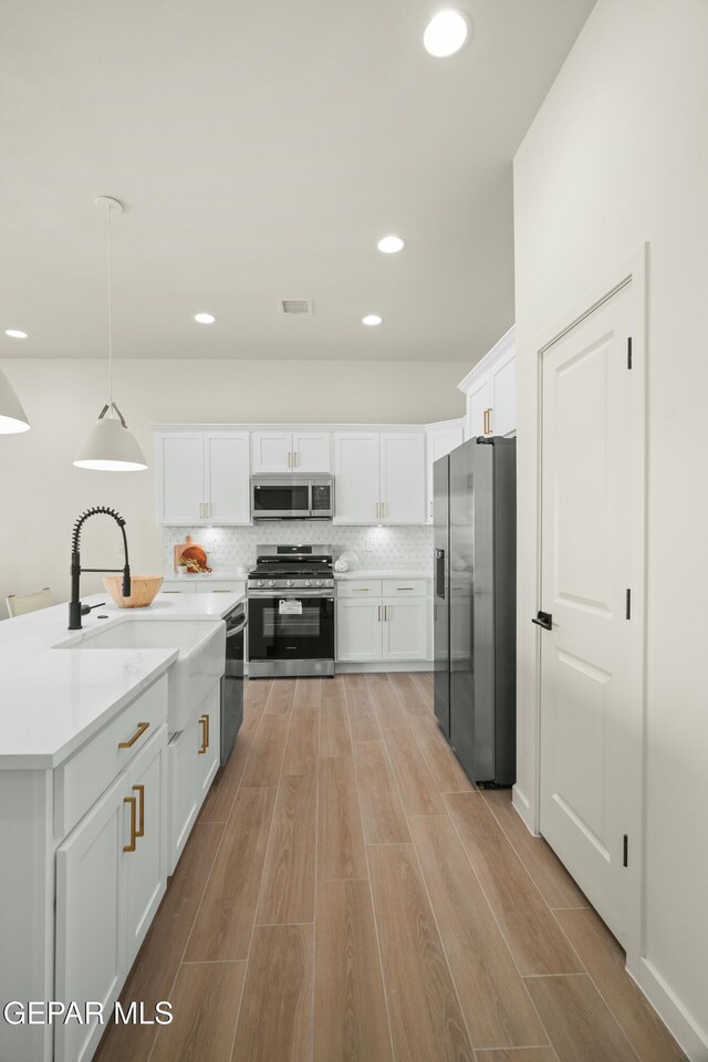 kitchen with white cabinetry, hanging light fixtures, stainless steel appliances, and sink