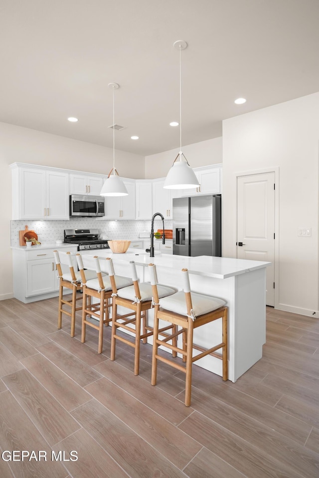 kitchen featuring white cabinetry, a kitchen island with sink, stainless steel appliances, and decorative light fixtures