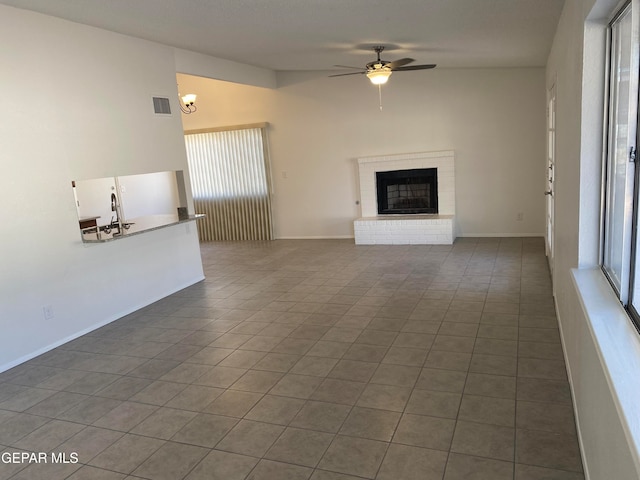 unfurnished living room with dark tile patterned flooring, ceiling fan, and a brick fireplace