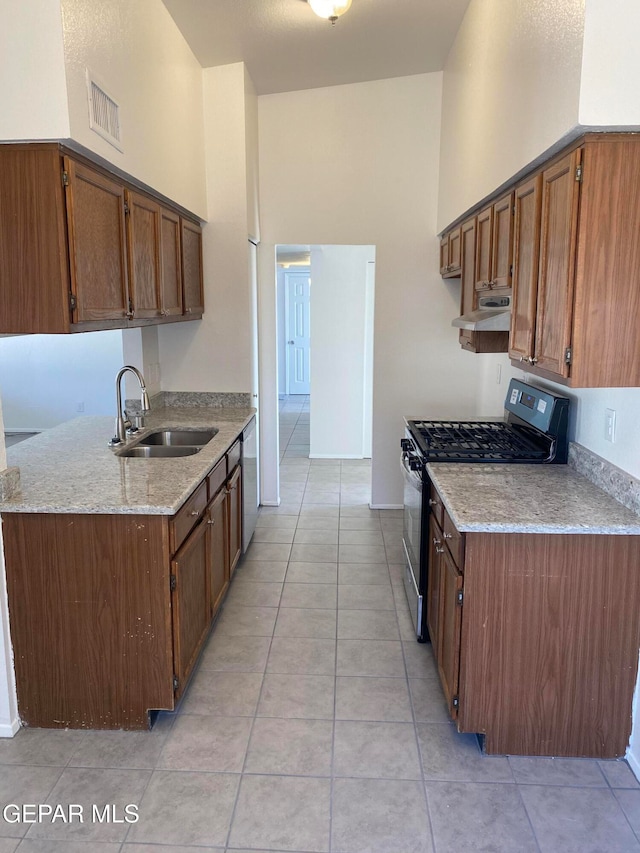 kitchen with sink, stainless steel appliances, a high ceiling, light stone counters, and light tile patterned floors