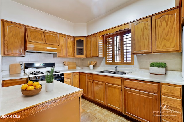 kitchen with light parquet floors, premium range hood, backsplash, gas range, and sink