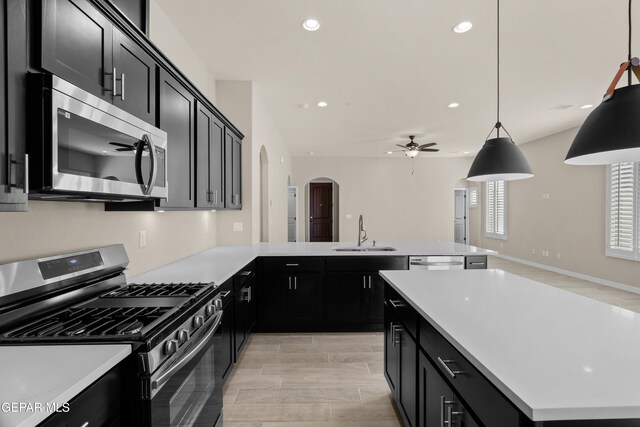 kitchen with appliances with stainless steel finishes, sink, light wood-type flooring, a center island, and decorative light fixtures