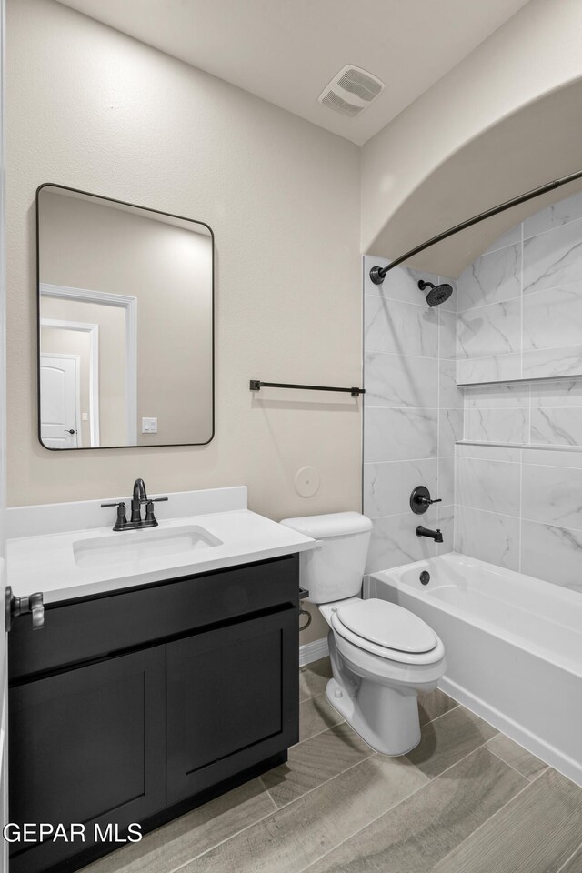 full bathroom featuring vanity, tiled shower / bath, and toilet