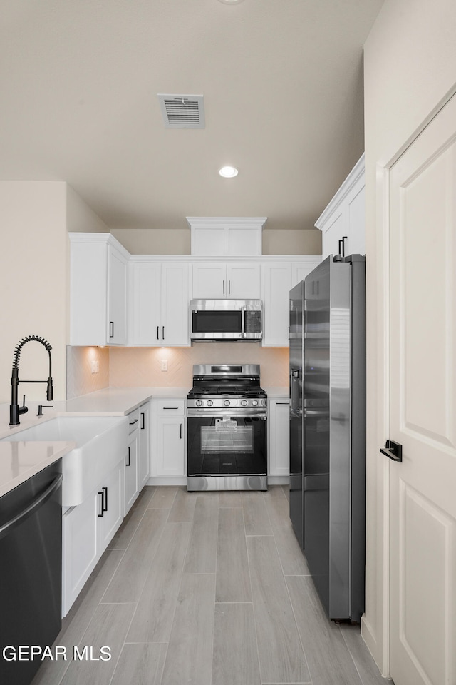 kitchen with tasteful backsplash, white cabinetry, light hardwood / wood-style flooring, sink, and stainless steel appliances