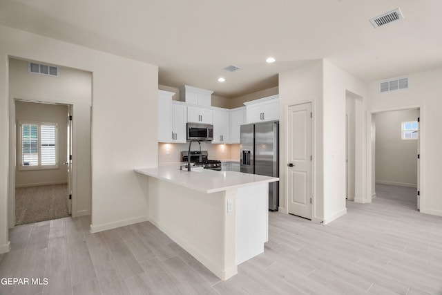 kitchen with kitchen peninsula, backsplash, white cabinets, appliances with stainless steel finishes, and light hardwood / wood-style floors