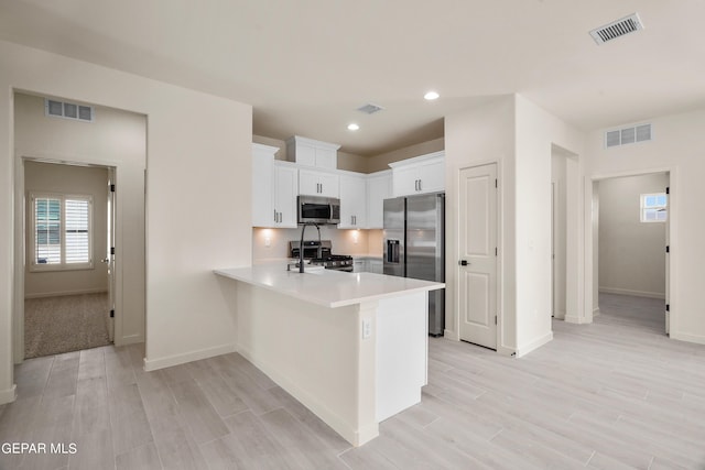 13870 Paseo Central Ave, Horizon City, TX 79928 - kitchen with appliances with stainless steel finishes, a peninsula, light countertops, light wood-type flooring, and white cabinetry