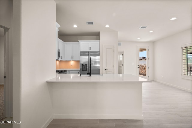 kitchen featuring appliances with stainless steel finishes, kitchen peninsula, white cabinetry, and light hardwood / wood-style floors