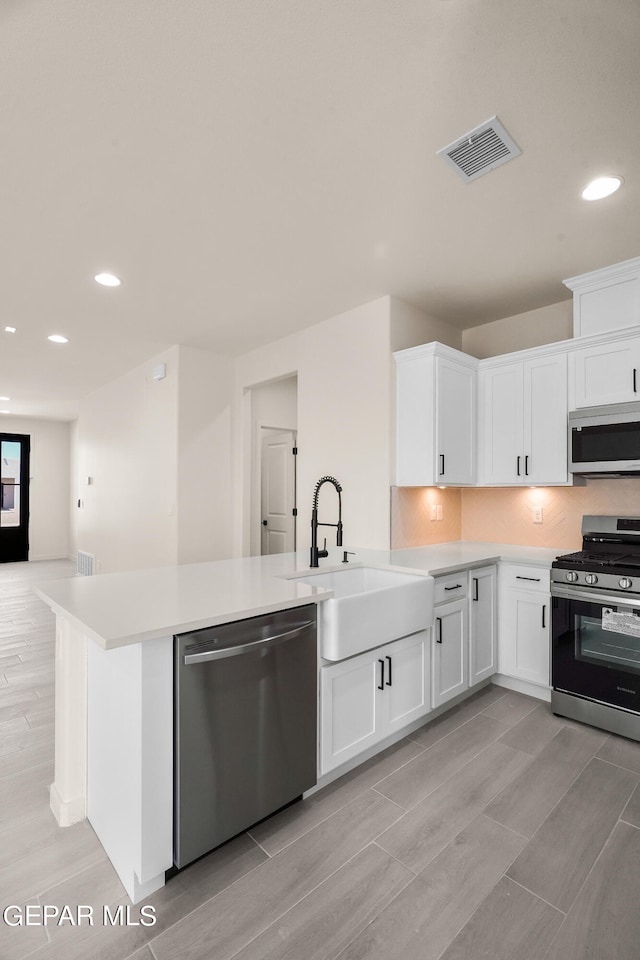 kitchen featuring appliances with stainless steel finishes, sink, light wood-type flooring, white cabinets, and decorative backsplash