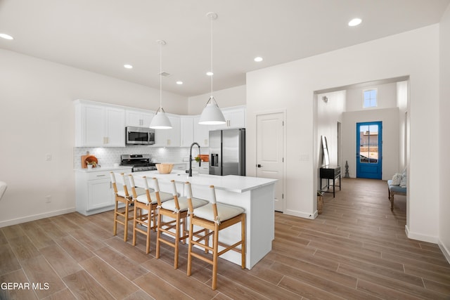 kitchen featuring appliances with stainless steel finishes, white cabinetry, light hardwood / wood-style floors, pendant lighting, and a center island with sink