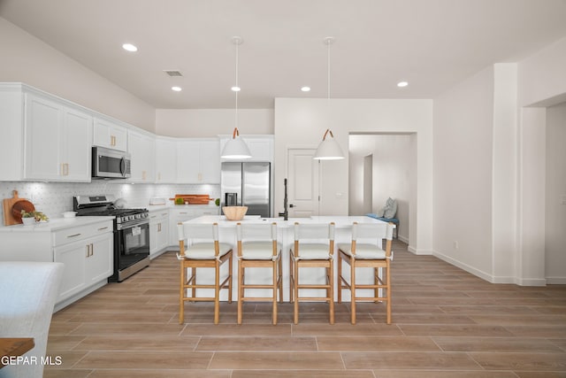 kitchen featuring white cabinetry, a kitchen island with sink, light hardwood / wood-style floors, decorative light fixtures, and stainless steel appliances